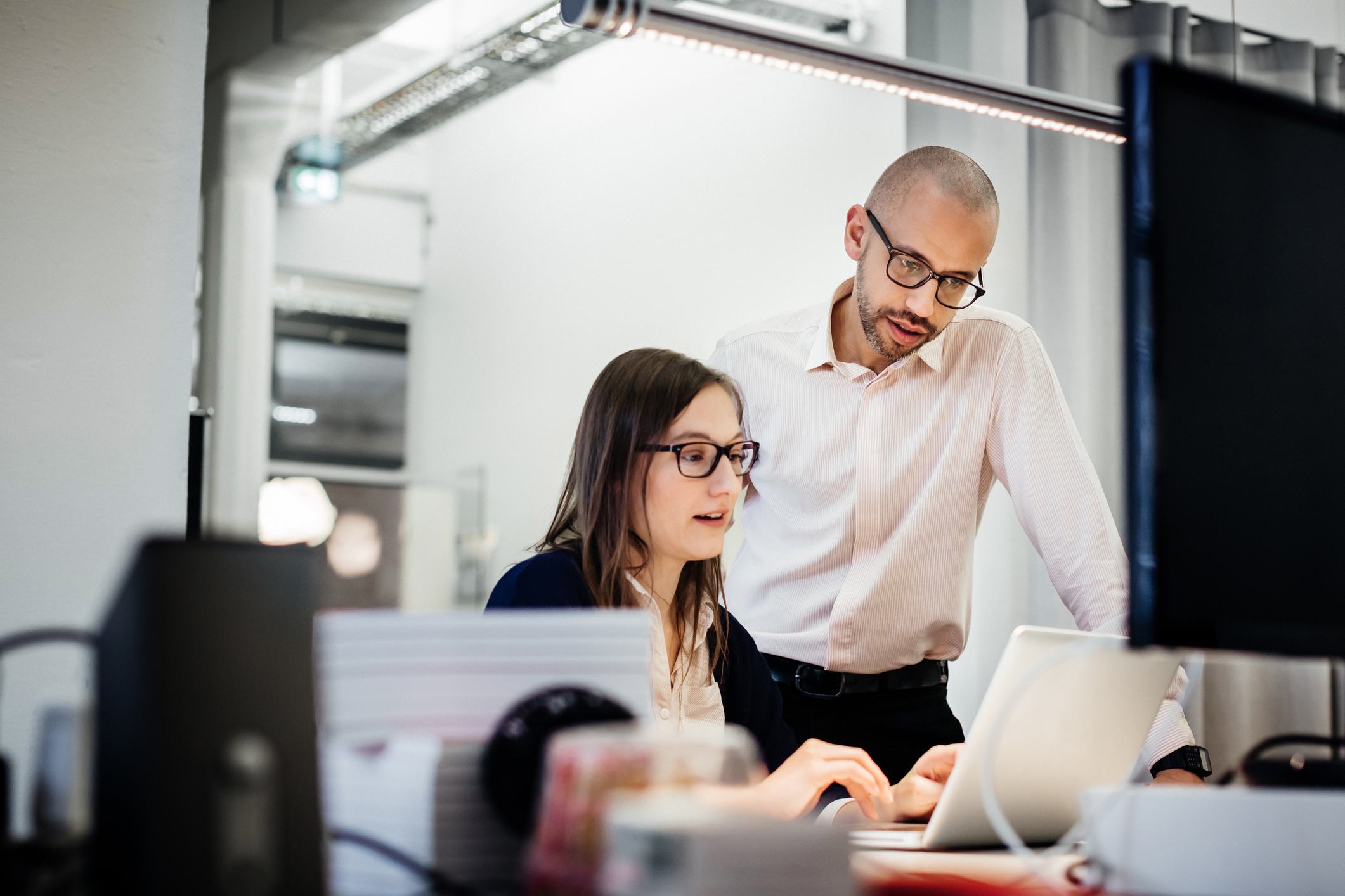 Woman working on laptop with man standing behind her pointing